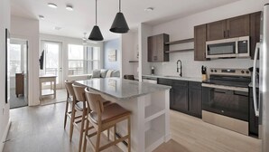 A modern kitchen with a central island, dark cabinetry, stainless steel appliances, and a view to the living area. - Landing | Stunning 1BD, Clubhouse, Gym (Little Rock)