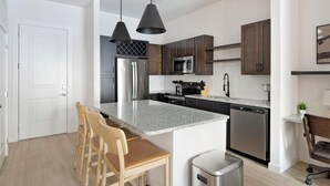 A modern kitchen with granite countertops, stainless steel appliances, and wooden bar stools. - Landing | Incredible 1BD, Clubhouse, Gym (Little Rock)
