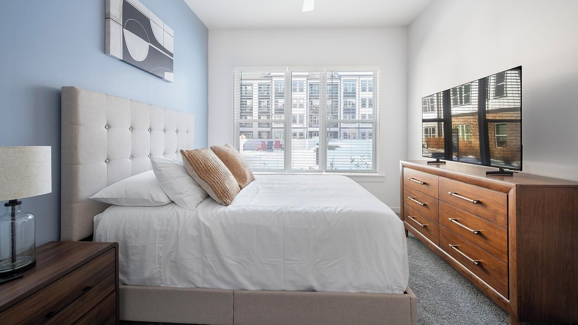 Una camera da letto con un letto, una cassettiera, una TV e una finestra con vista sulla città.