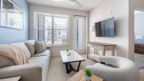 Ein modernes Wohnzimmer mit Sofa, Ohrensessel, Couchtisch und einem an der Wand befestigten Fernseher.