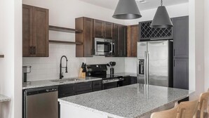 A modern kitchen with dark wooden cabinets, stainless steel appliances, a granite countertop, and pendant lighting. - Landing | Beautiful 1BD, Clubhouse, Gym (Little Rock)