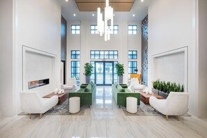 A spacious lobby with high ceilings, large windows, and a central seating area with green sofas and white armchairs. - Landing | Stylish 1BD, Gym, Courtyard (Little Rock)