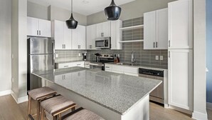 A modern kitchen with white cabinetry, a granite countertop, stainless steel appliances, and a central island with bar stools.