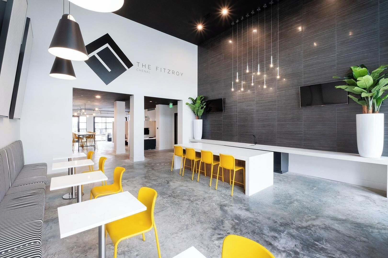 A modern interior with a reception desk, yellow chairs, and a grey-tiled wall.