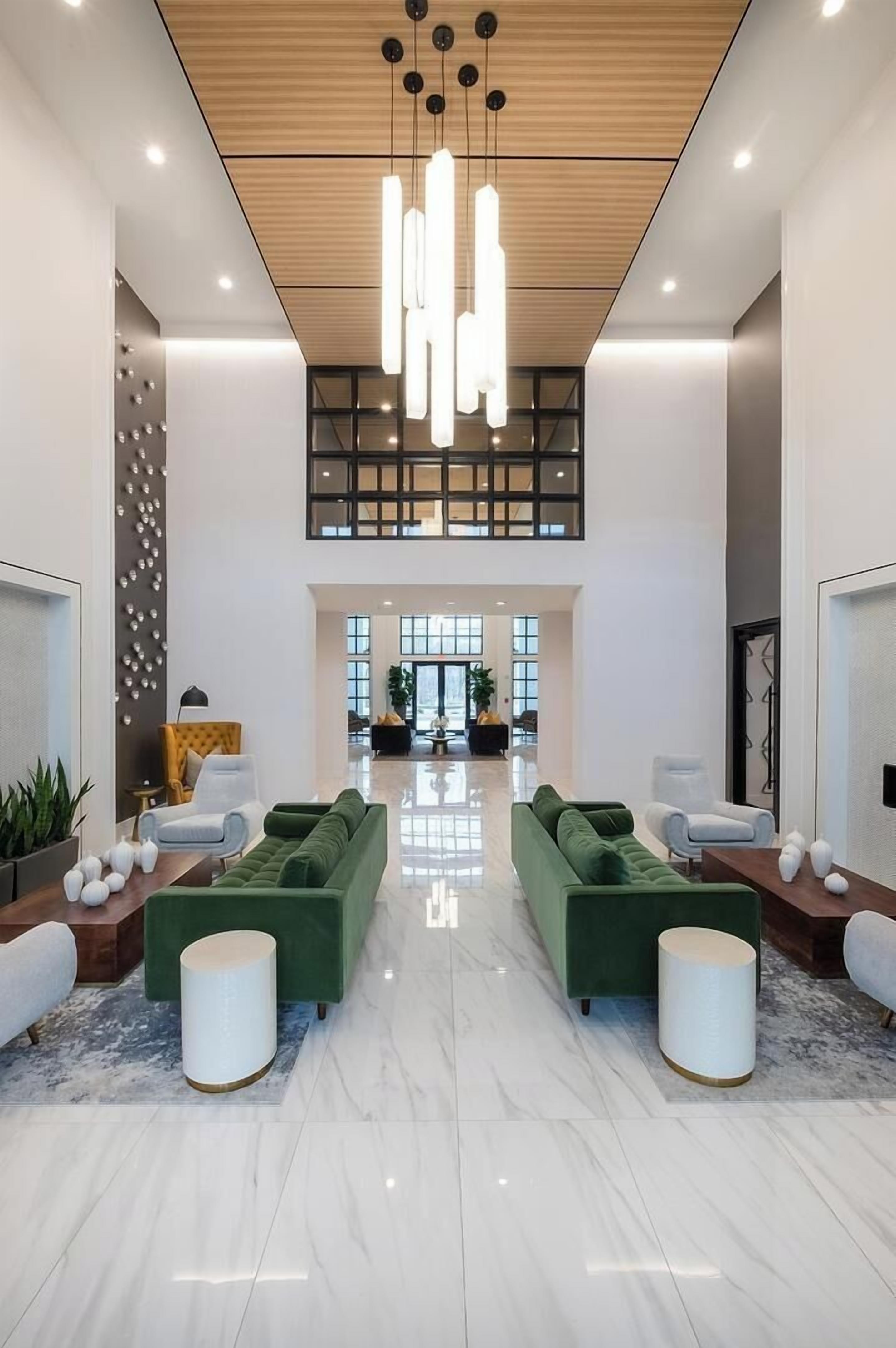 A spacious lobby with a high ceiling, modern pendant lighting, green sofas, and a marble floor.