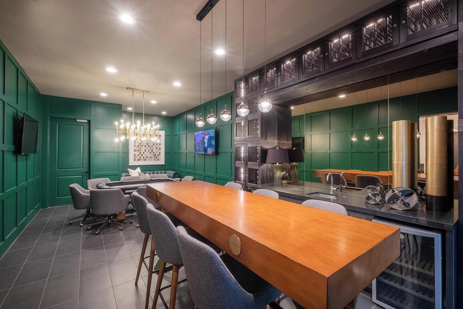 A modern conference room with a long wooden table, grey chairs, a television, and a kitchen area with a stove and refrigerator.