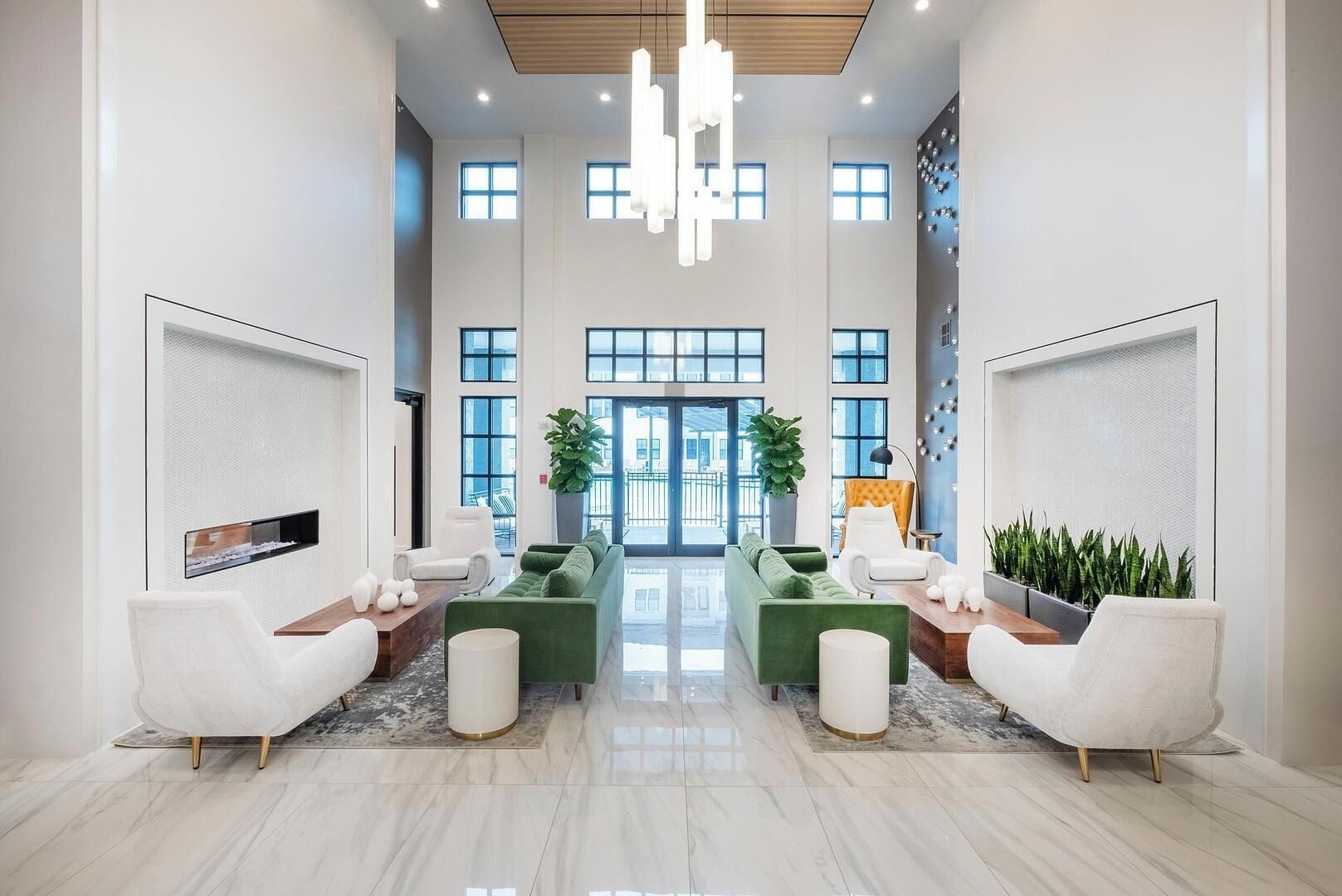 Un vestíbulo amplio con techos altos, ventanas grandes y una zona de estar central con sofás verdes y sillones blancos.