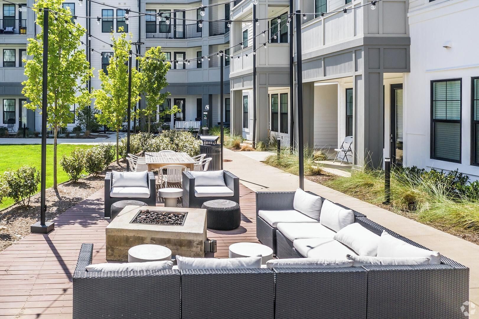 Un patio moderno al aire libre con mobiliario de mimbre, un hogar para fogata y vista a un edificio de varios pisos.