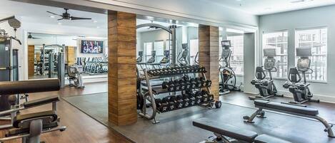 Une salle de sport équipée de machines de cardio, de supports à poids et de bancs.