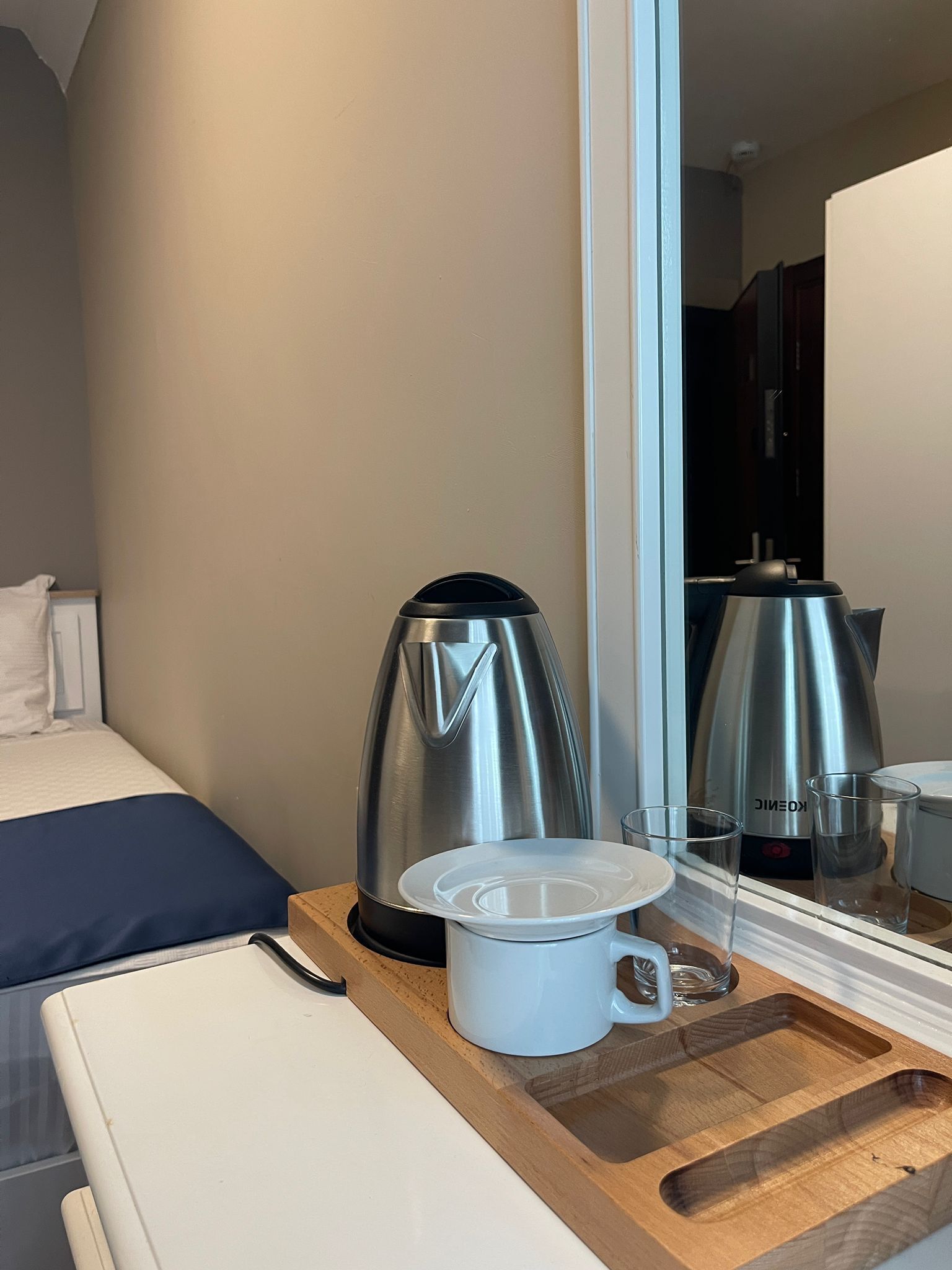Hotellihuone, jossa on sänky, puinen yöpöytä, kahvinkeitin, muki ja lasi.