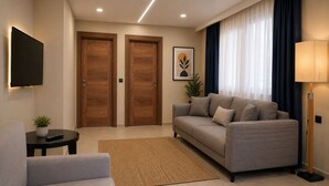 Una sala de estar moderna con un sofá, una mesita con una planta, un televisor montado en la pared y dos puertas de madera.