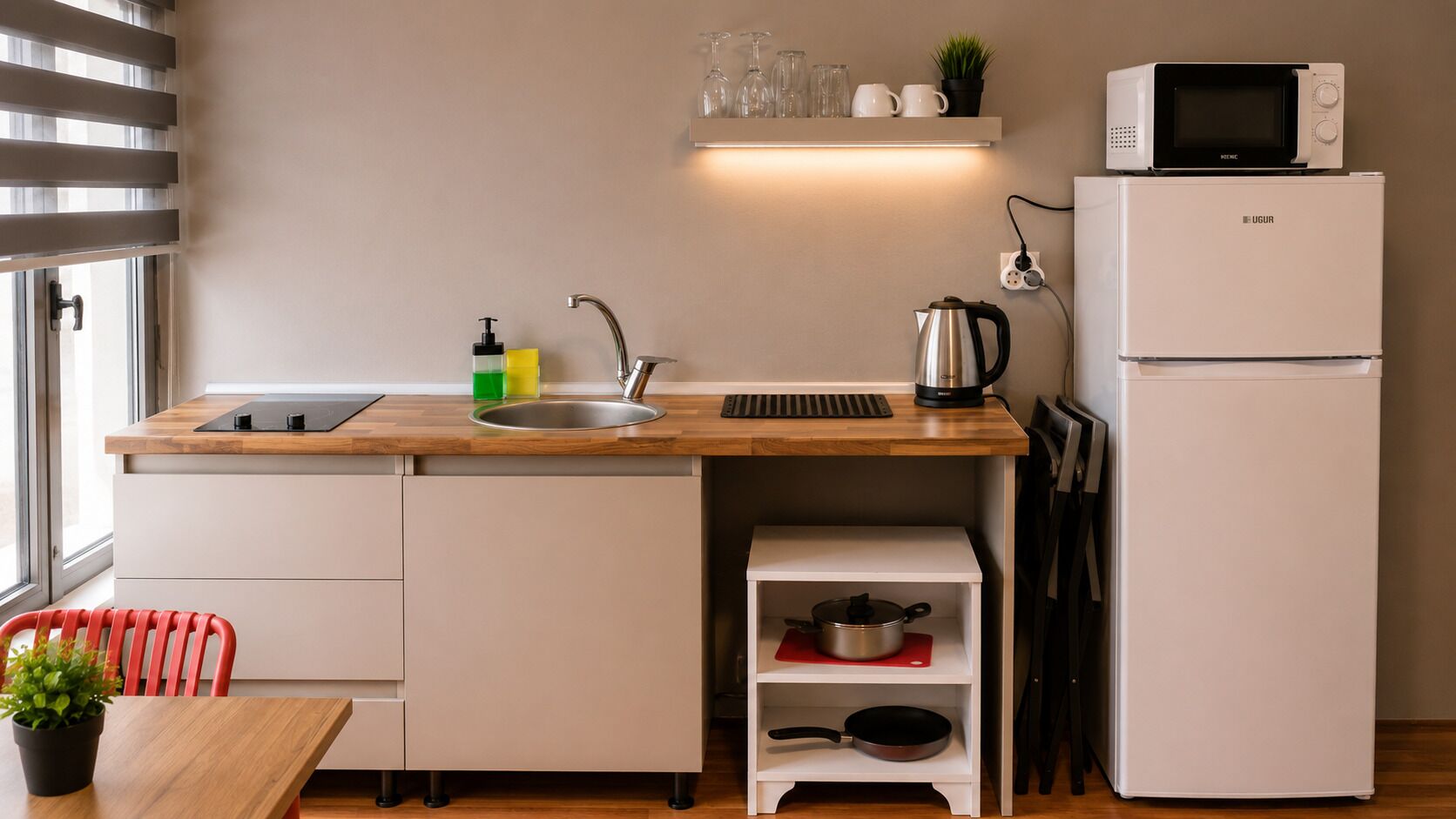 Cocina compacta con lavabo, microondas, hervidor y una pequeña estantería con utensilios de cocina.