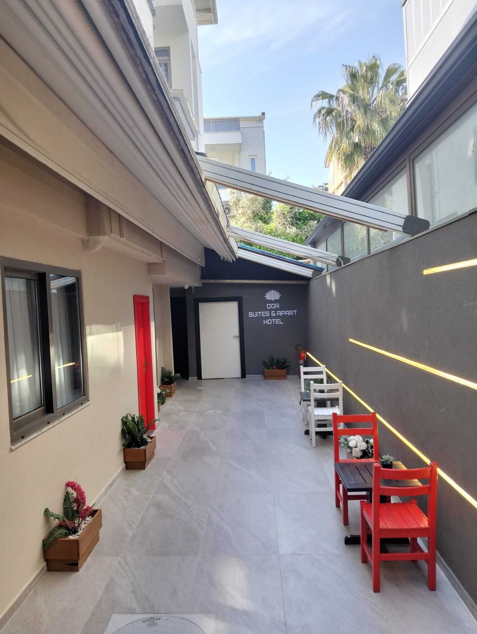Un couloir d’hôtel avec un plafond en verre, une porte rouge et une enseigne indiquant « DOA SUITES & APART HOTEL ».