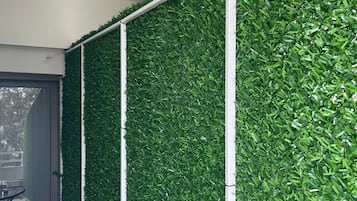 A corridor with green artificial foliage walls, a ceiling-mounted smoke detector, and a door leading to an outdoor area.