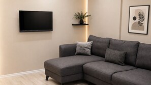 Una sala de estar con un sofá modular, un televisor de pantalla plana, una planta y una obra de arte enmarcada en la pared.