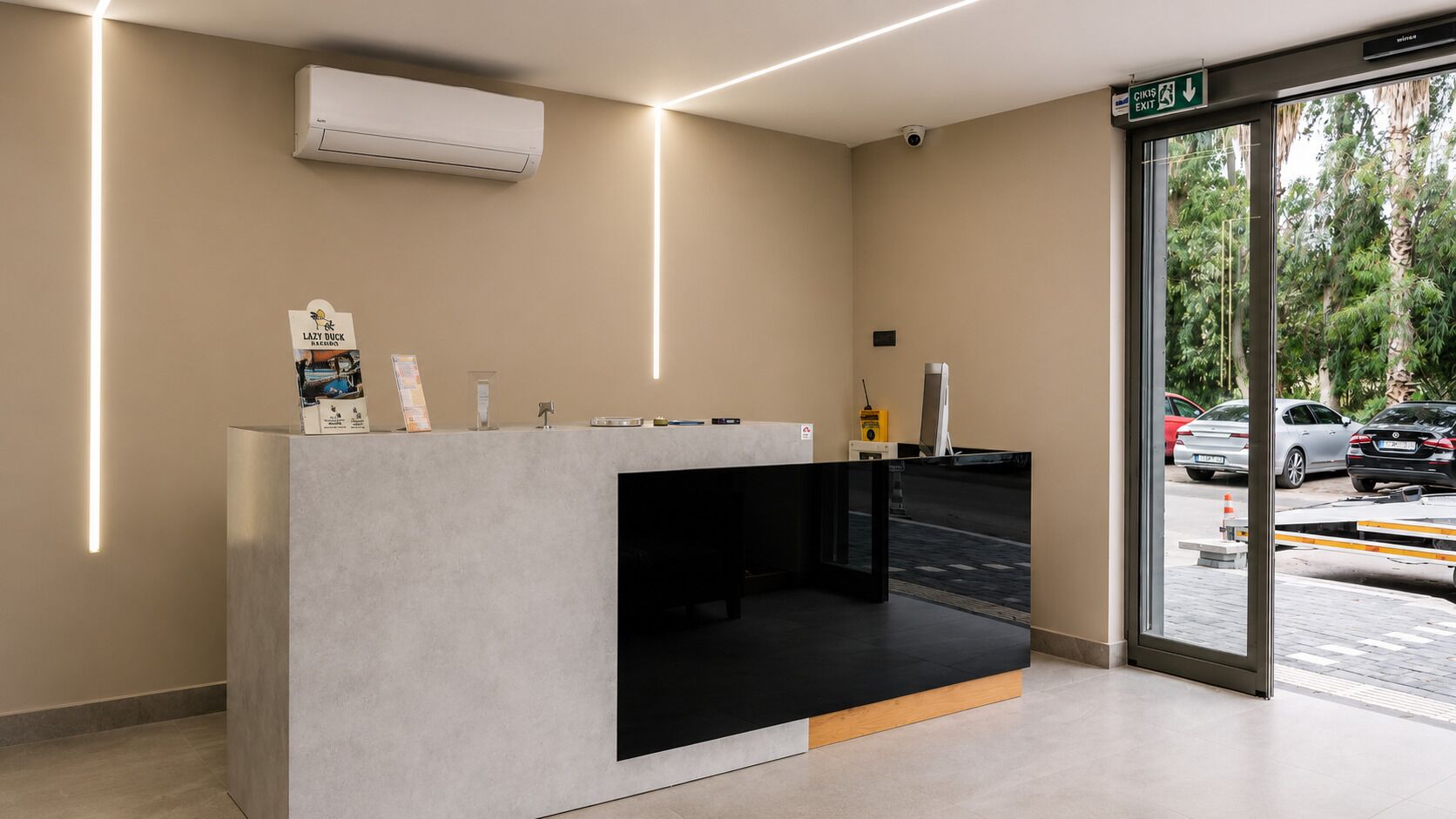 A reception desk with a modern design, an air conditioning unit above it, and a view of parked cars outside.