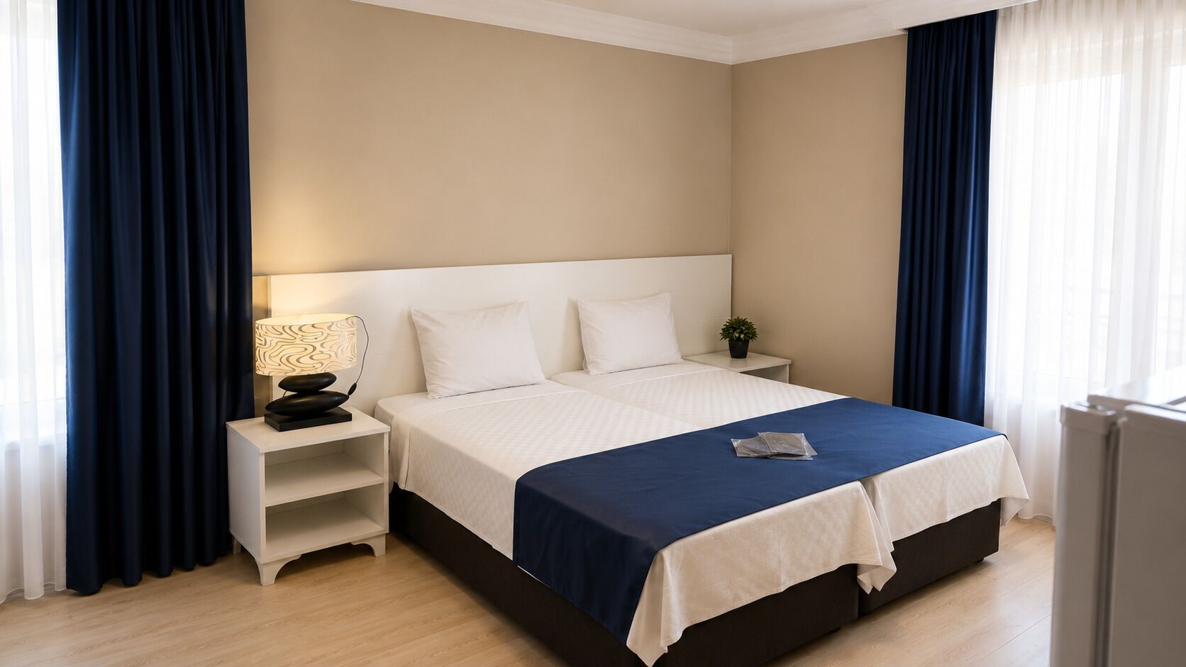 A hotel room with a bed, bedside table, lamp, and a small potted plant.