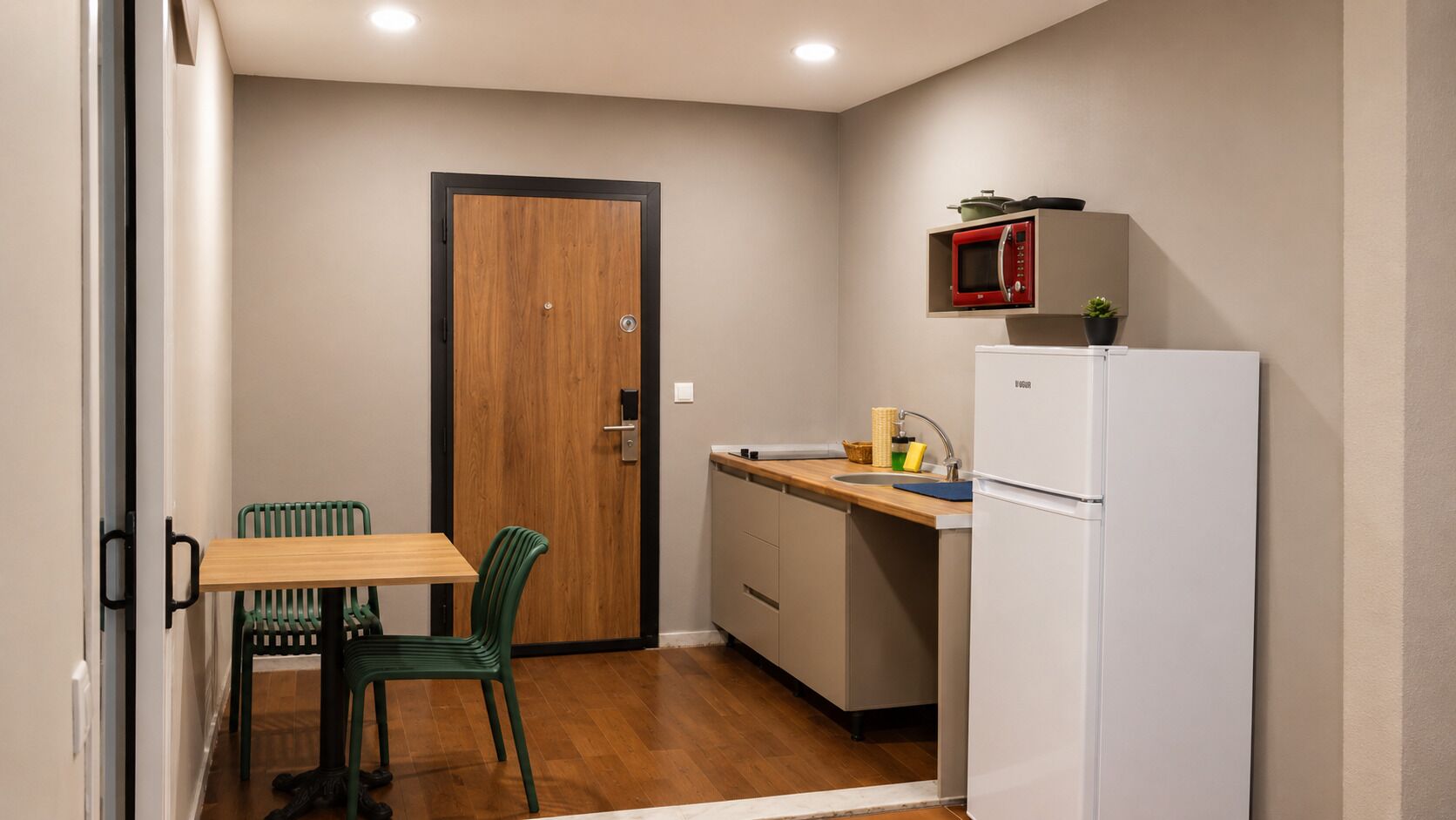 A compact kitchen with a wooden door, a small dining table with chairs, a microwave, and a refrigerator.
