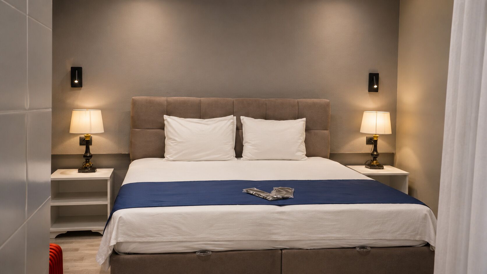 A neatly made bed with a blue accent, two bedside lamps, and a wall-mounted light fixture.