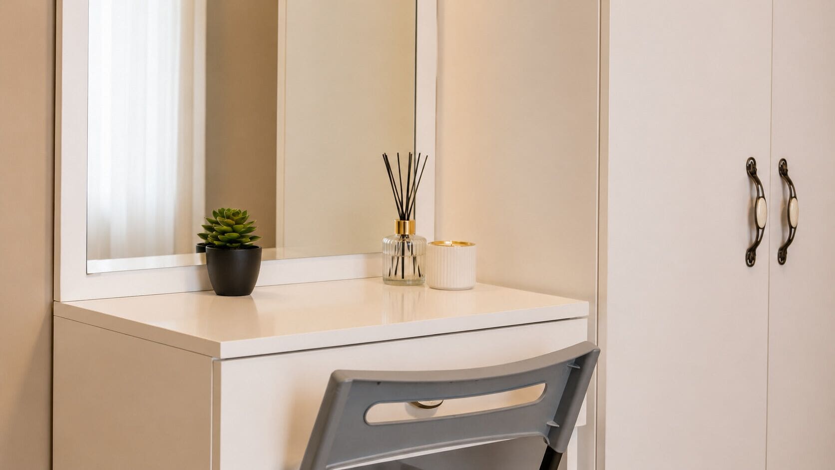 A white vanity with a mirror, a potted plant, and a candle holder.