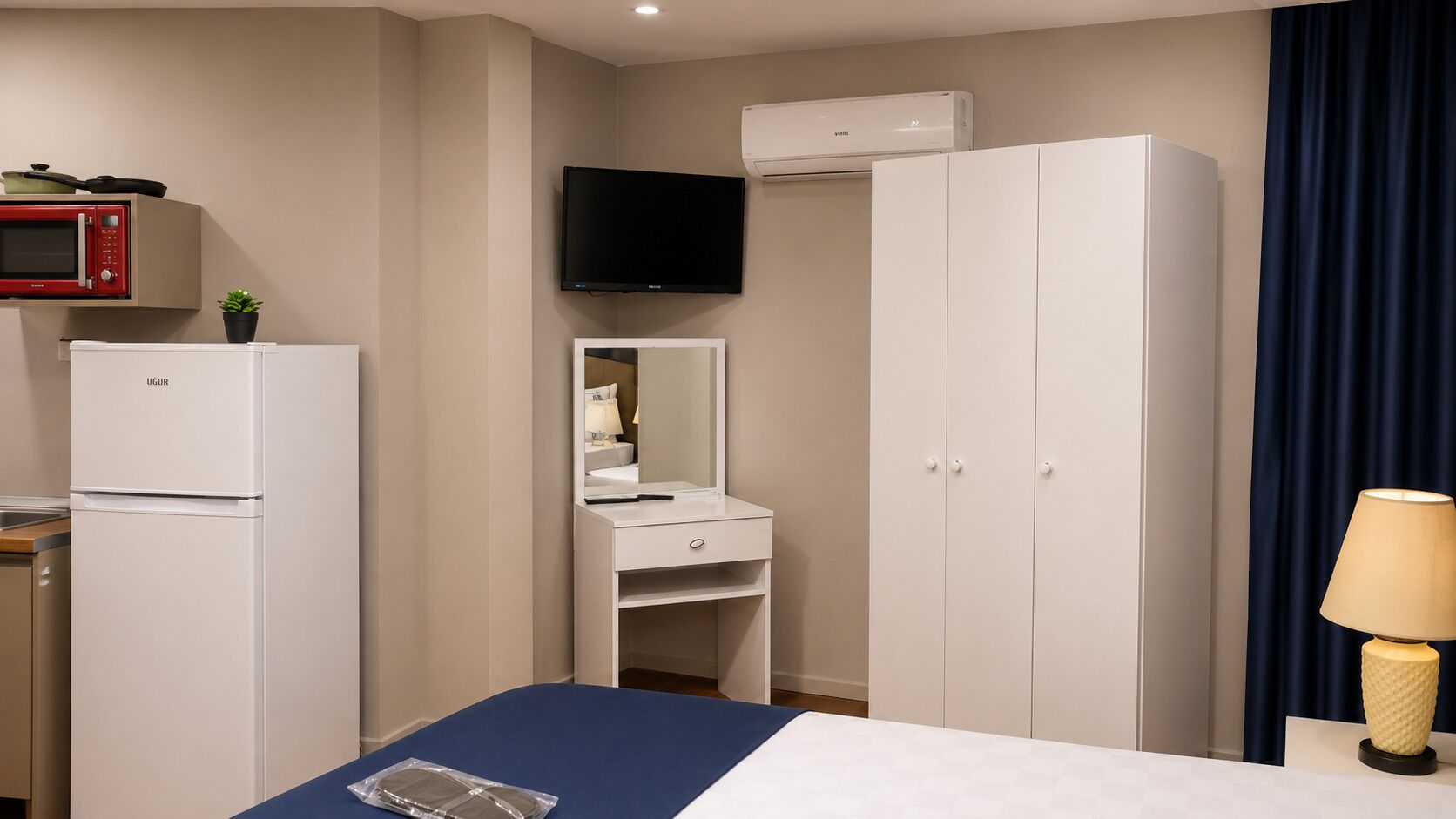 A hotel room with a bed, a desk with a mirror, a wardrobe, a microwave, and an air conditioner.