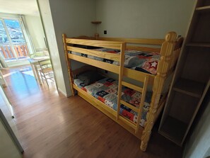 En våningssäng med ett quiltat överkast, ett trägolv och utsikt över en balkong.