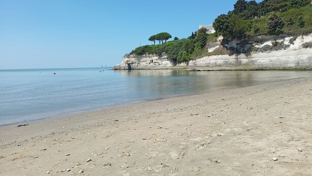 A beach with a rocky shoreline, a clear sky, and a building on a cliff.