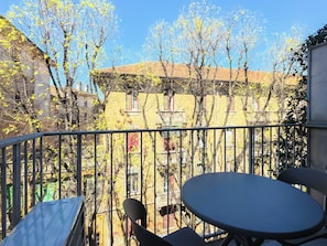 A balcony with a table and chairs, overlooking a courtyard with trees and buildings. - Milano Apartments Barbavara 7A (Milan)