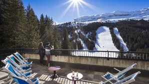 Eine Terrasse mit Liegestühlen und einem Tisch, mit Blick auf eine verschneite Berglandschaft.