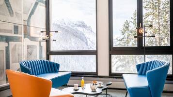 A modern room with large windows, two blue armchairs, an orange chair, a coffee table, and a radiator.