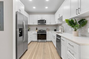 A modern kitchen with white cabinetry, stainless steel appliances, and a wooden floor.