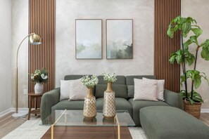 A living room with a green sofa, two vases with flowers, a floor lamp, and a large plant.