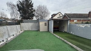A backyard with artificial grass, a table, and a chair. - Charming Bungalow Rental in Rainham Comfort and Convenience (Rainham)