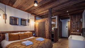 A bedroom with a large bed, a wooden ceiling, a bathroom with a bathtub, and a wooden wall panel. - Chalet Genepy by Interhome (Peisey-Nancroix)