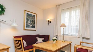 A room with a wooden table, a red sofa, a wooden chair, a lamp, a picture on the wall, and a window with curtains. - 4 Person Holiday Home in Brovst (Brovst)