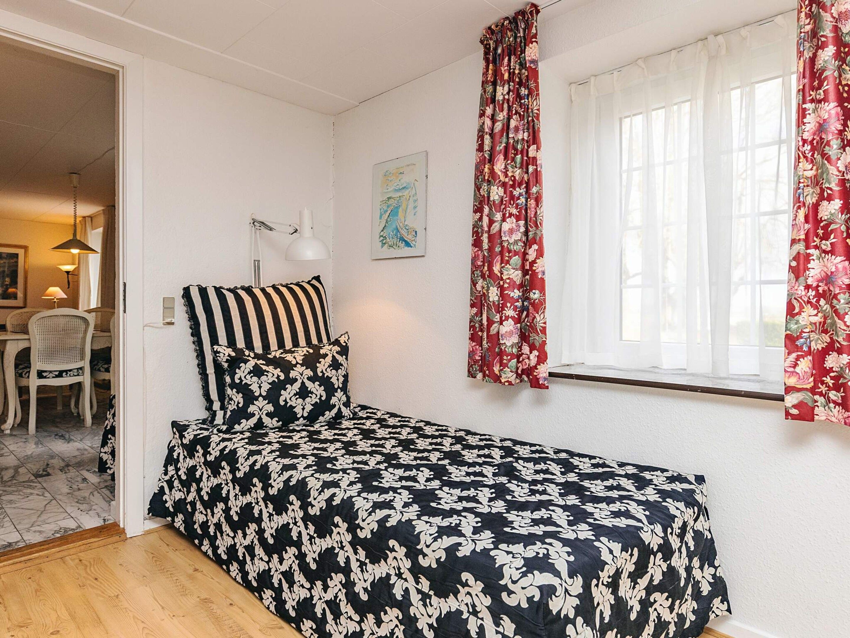 A bedroom with a bed, a desk, a chair, and a window with curtains.