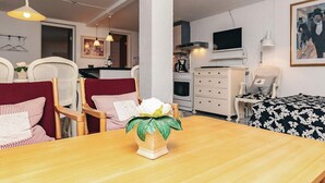 A dining area with a wooden table, chairs, a vase with a flower, a kitchen in the background, and a television on the wall. - 4 Person Holiday Home in Brovst (Brovst)