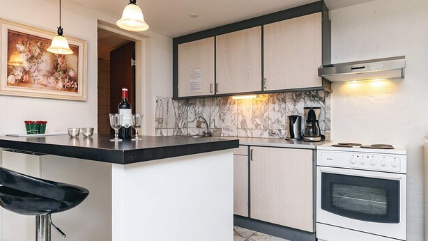 A kitchen with a marble backsplash, a built-in oven, and a bar area with stools. - 4 Person Holiday Home in Brovst (Brovst)