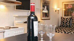 A bottle of wine on a table with two glasses, a kitchen in the background, and a patterned sofa. - 4 Person Holiday Home in Brovst (Brovst)