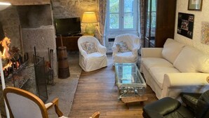 A cozy living room with a stone fireplace, a television, a sofa, and a coffee table. - Relaxation and space in a family home with breathtaking views! (Ambrugeat)