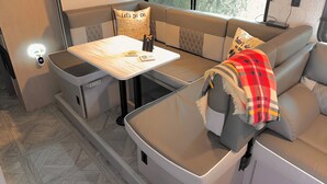 Un intérieur de camping-car compact comprenant une table à manger, des sièges rembourrés et une fenêtre offrant une vue sur l’extérieur.