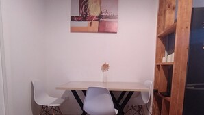 A dining area with a wooden table, four white chairs, a vase with a flower, and a painting on the wall.