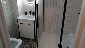 A bathroom with a shower, toilet, sink, and a circular mirror.