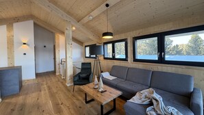 Un interno moderno con pavimento in legno, un divano grigio, un tavolo in legno e un'ampia finestra vista alberi.