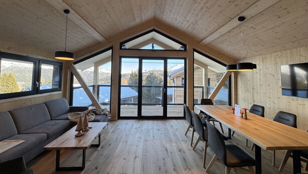 Un interno moderno con soffitto in legno, ampie finestre, zona pranzo e divano.