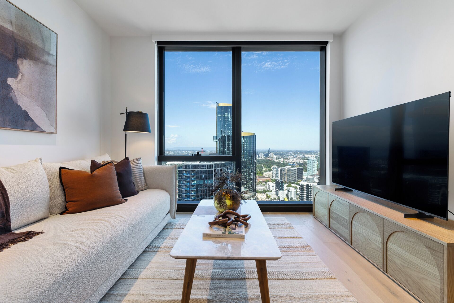 A modern living room with a large window, a sofa, a coffee table, and a flat-screen TV.
