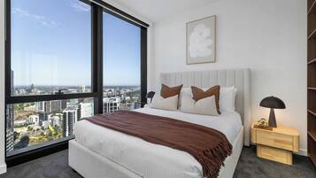 A bedroom with a large window, a bed with pillows, a bedside table, and a wall-mounted artwork.