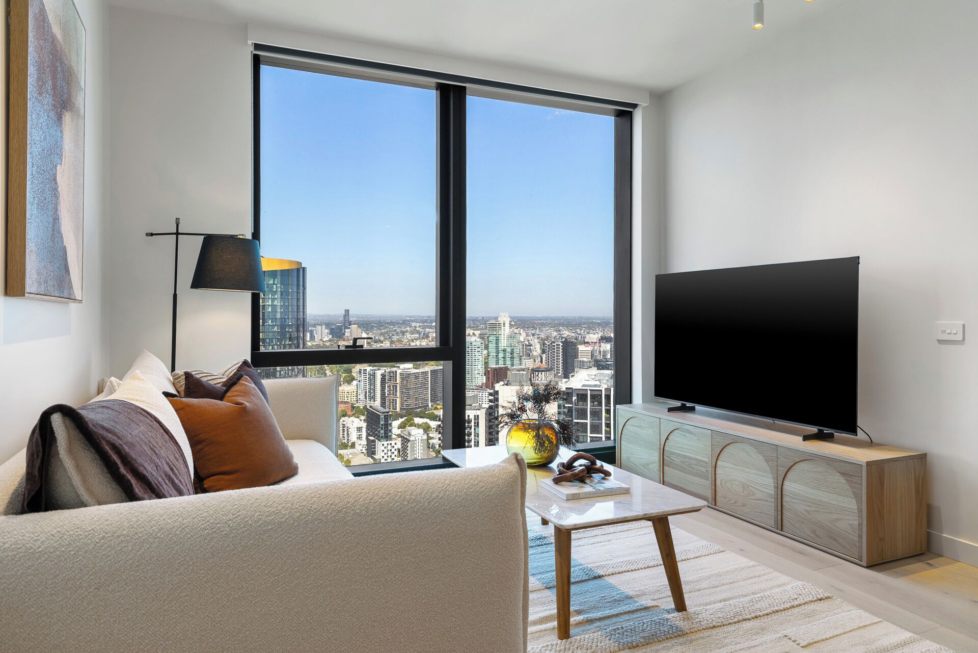 A modern living room with a large window, a flat-screen TV, a sofa, a coffee table, and a cabinet.
