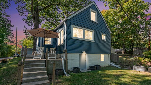 A two-story house with a covered porch, a set of stairs leading to the entrance, and a small front yard. - Dogs Stay Free! Lakefront Home near Notre Dame (South Bend)