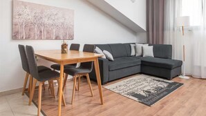 A modern living room with a dining table, grey sofa, and a cityscape artwork on the wall. - Seaview Family Villa With Heated Pool (Okrug)